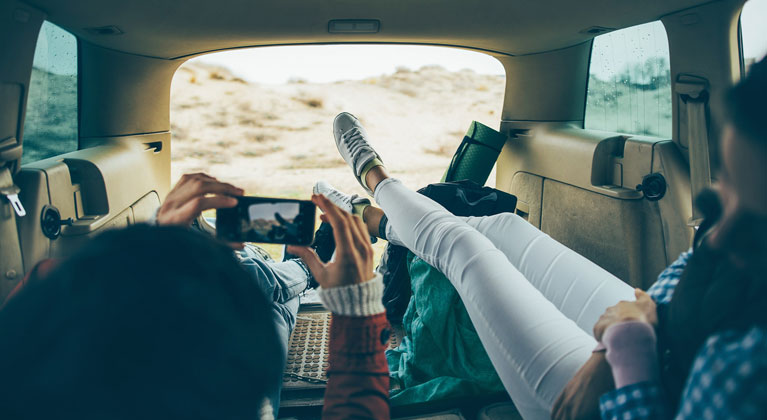 Couple laying in the back of car overlooking sand dunes and taking photos.