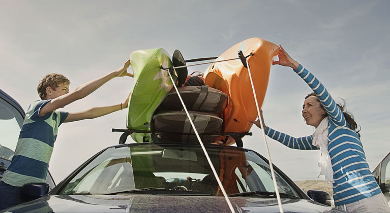 Mother and son putting canoes on the top of their car.
