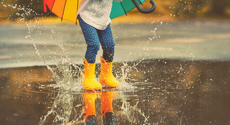 Child splashes orange wellies in a puddle.