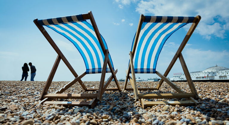 2 striped deckchairs on a pebble beach in the sunshine.