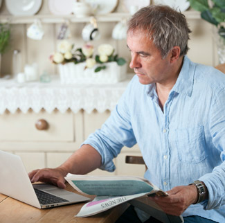 Man holding a newspaper and looking at a laptop