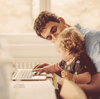 Man with child on knee looking at laptop