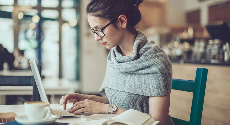 Woman works on laptop in a coffee shop.