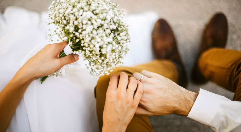 Close up of bride and groom holding hands.