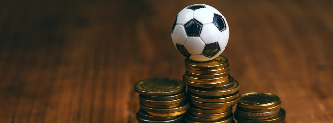 Miniature football balancing on stack of coins