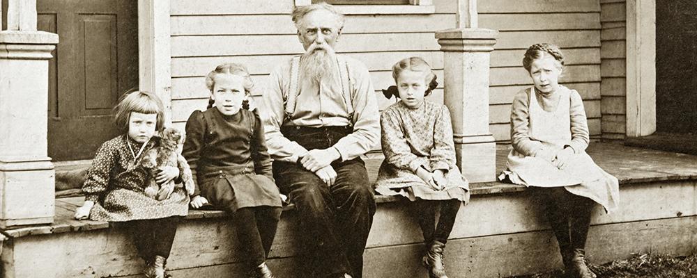 Grandfather and grandchildren sitting in front of house
