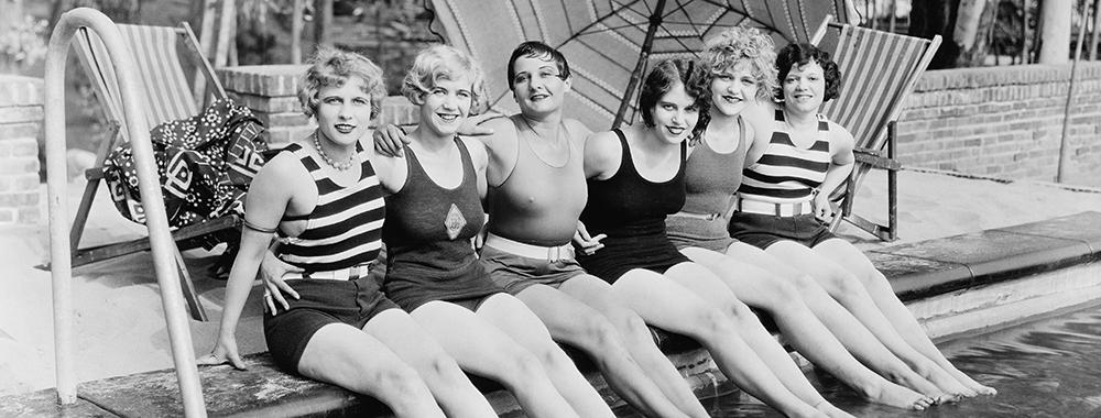 Row of six women sitting at the edge of a swimming pool