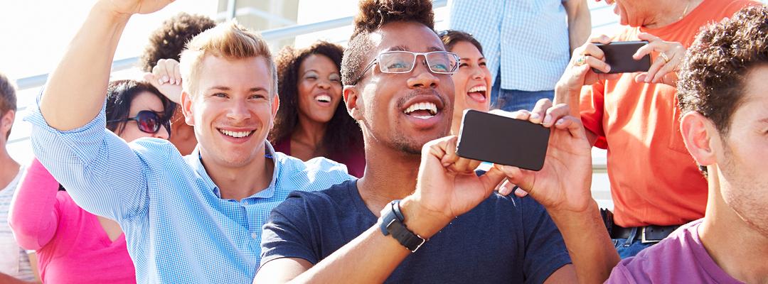 Men in crowd cheering taking photo with smartphone